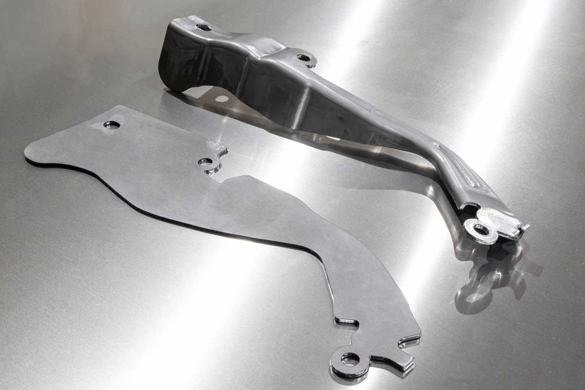 A flat steel blank beside the formed part produced from it at Prototier-1